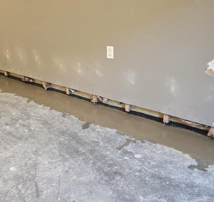 A partially repaired wall with missing lower drywall reveals wooden studs and insulation. Fresh concrete is visible along the base, conveying ongoing construction.
