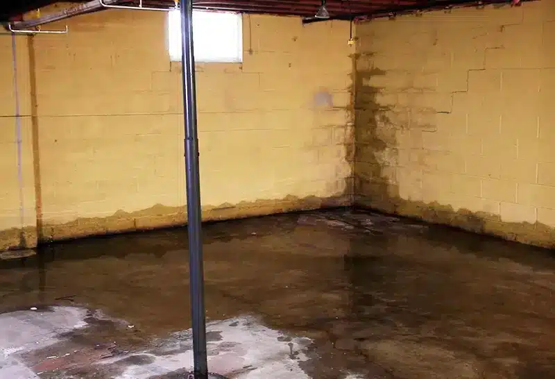 Wet basement floor with water intrusion and moisture stains along foundation walls