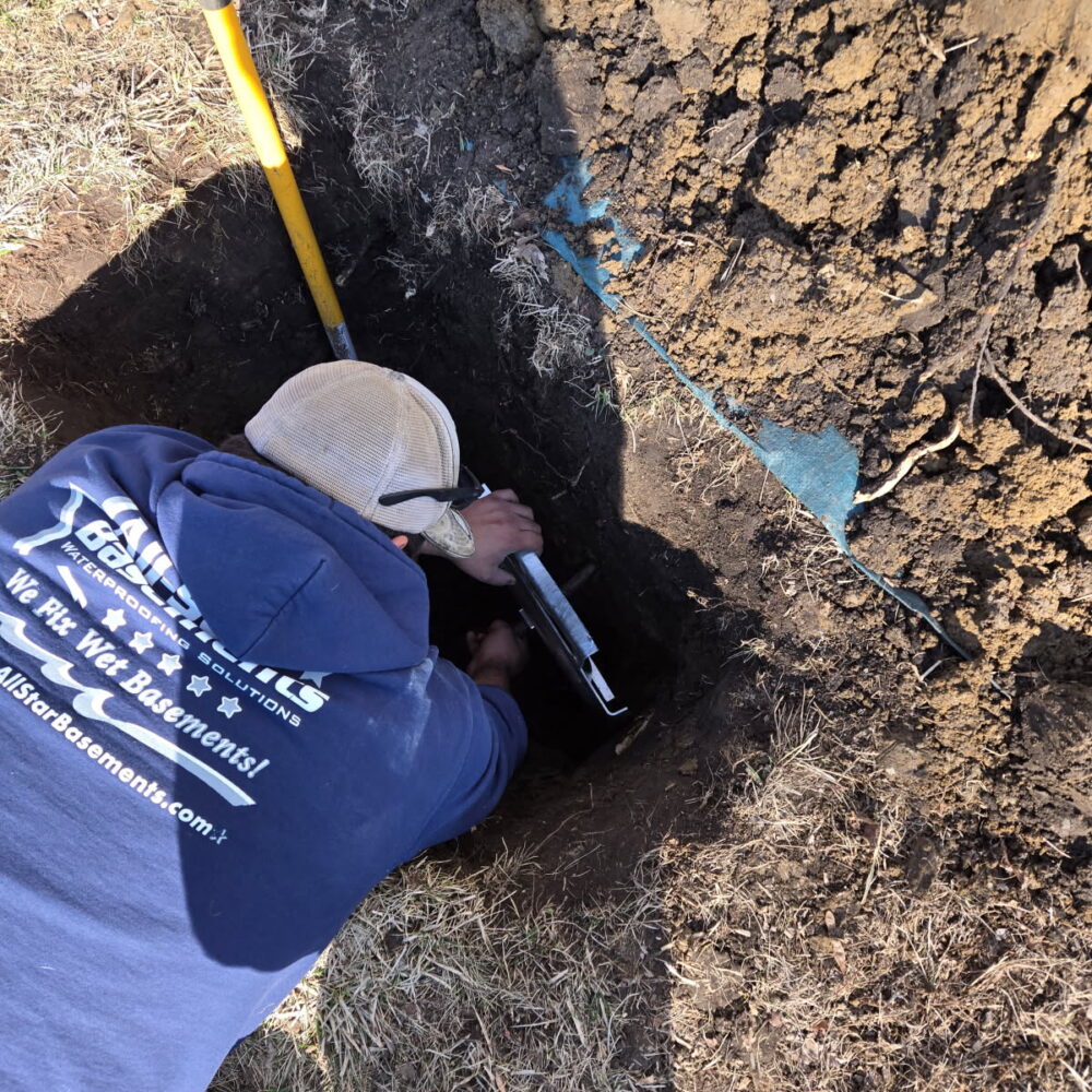 Technician installing foundation piers to repair signs of a sinking foundation during an exterior foundation stabilization project.